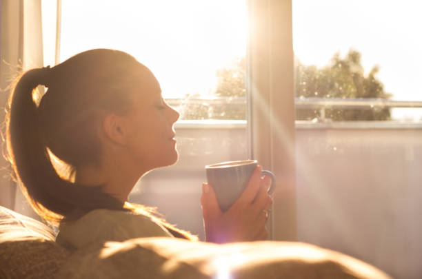 ragazza che annusa il caffè accanto alla finestra al mattino - waking up window women morning foto e immagini stock