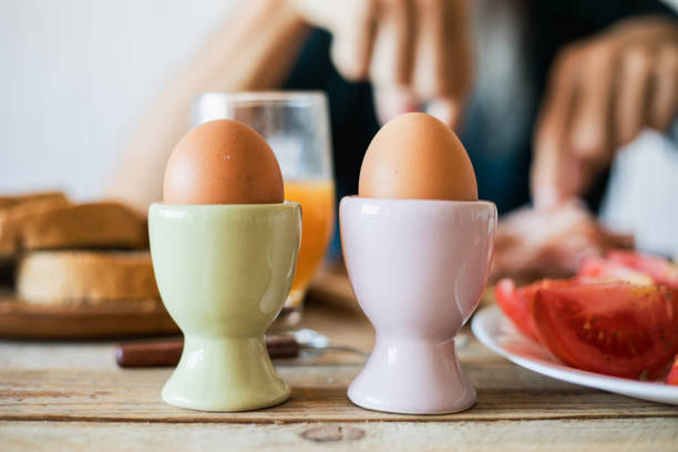 Breakfast at table - eggs with moratdella cow cheese and tomato Breakfast - boiled eggs in ceramic stands. Tomato and bread slices with unrecognizable man in background boiled egg photos stock pictures, royalty-free photos & images