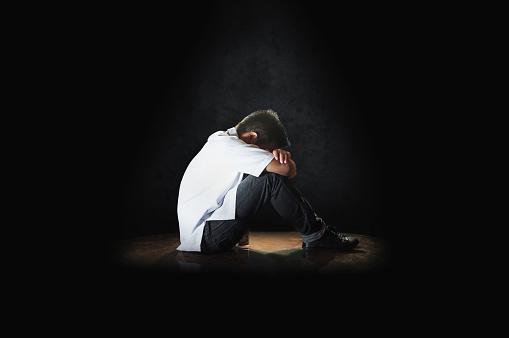A depressed student sitting on a floor with his head down crying. Depressed school boy in side view.