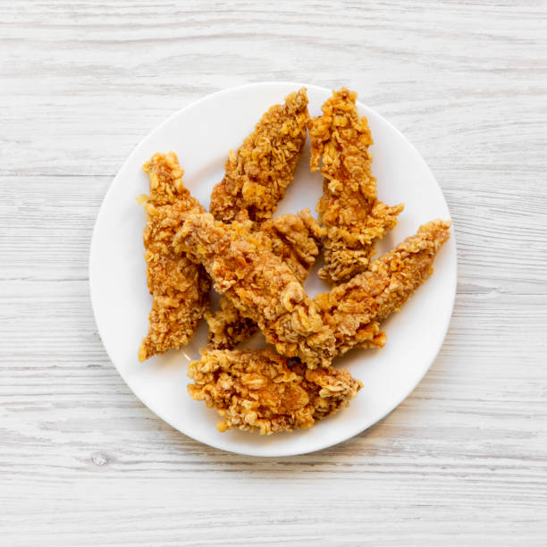 Spicy chicken strips on white plate over white wooden background, top view. Flat lay, from above, overhead. Spicy chicken strips on white plate over white wooden background, top view. Flat lay, from above, overhead. chicken finger stock pictures, royalty-free photos & images