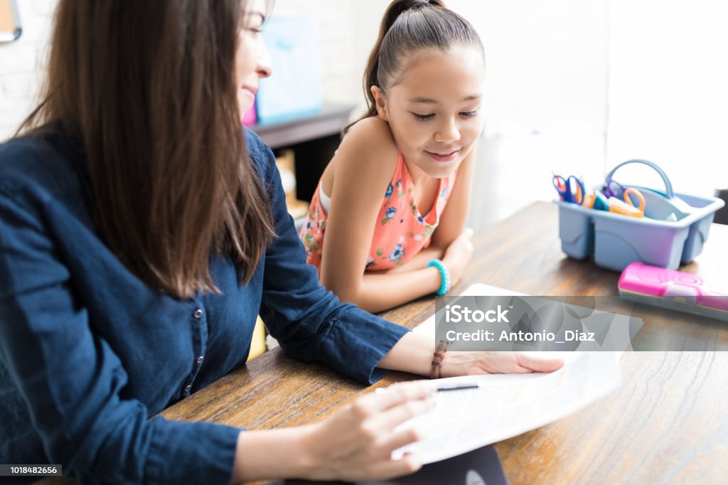Niña leyendo notas en manos de profesor en la mesa en casa - Foto de stock de Leer libre de derechos