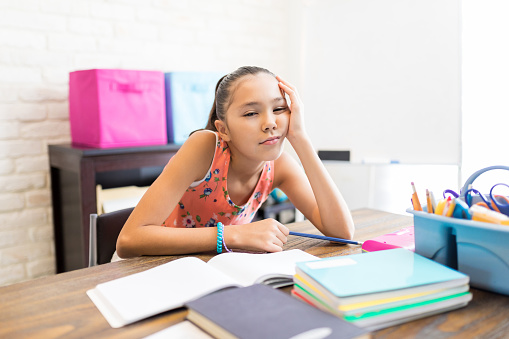 Girl tired of doing homework with books on table at home