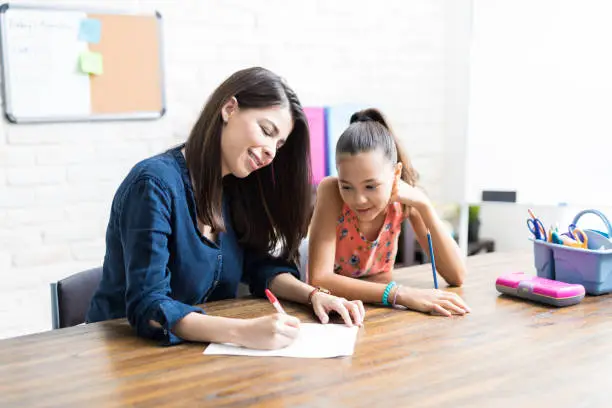 Homeschooling mother assisting daughter with schoolwork at table