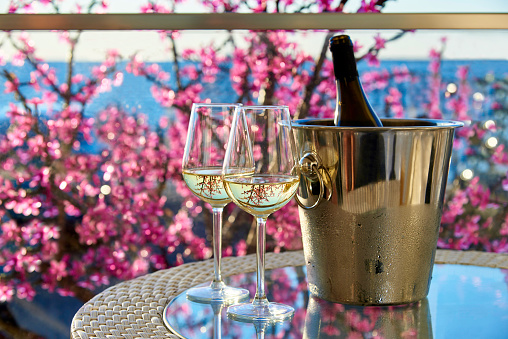 Two glasses of white cold wine on a glass table on the background of the sea and flowers.