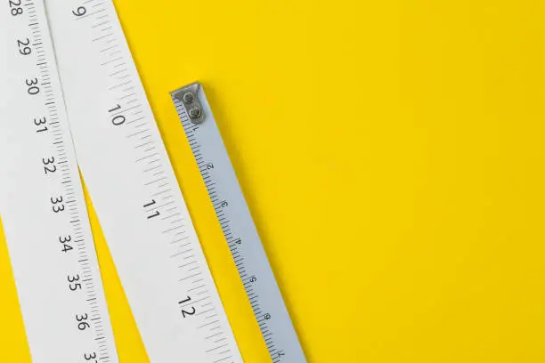 White measuring tapes with centimetre and inches on vivid yellow background with copy space, length, long or maker concept.