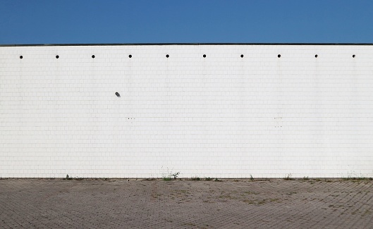 Urban background. Concrete road, a white wall  made of square bricks and blue sky .