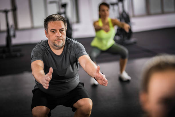 übergewicht im mittleren alter mann macht kniebeugen im aerobic-kurs - women sweat healthy lifestyle exercising stock-fotos und bilder