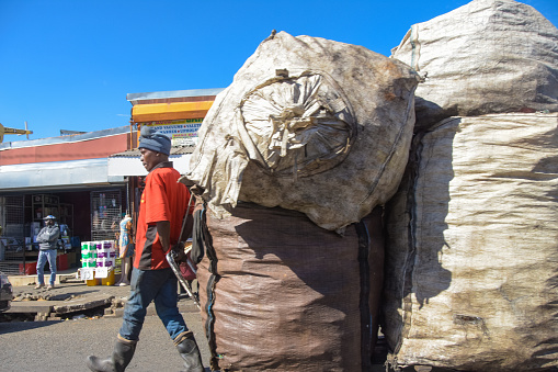 Johannesburg , Gauteng / South Africa -August 02 2018 : African male waste picker working , large carry bag with recyclables, daytime on the streets ,horizontal shot, walking to destination,