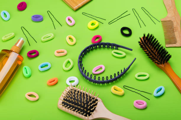 on a light green background, scattered objects to create hairstyles, elastic band of different colors, and a comb, and a spray for styling.
