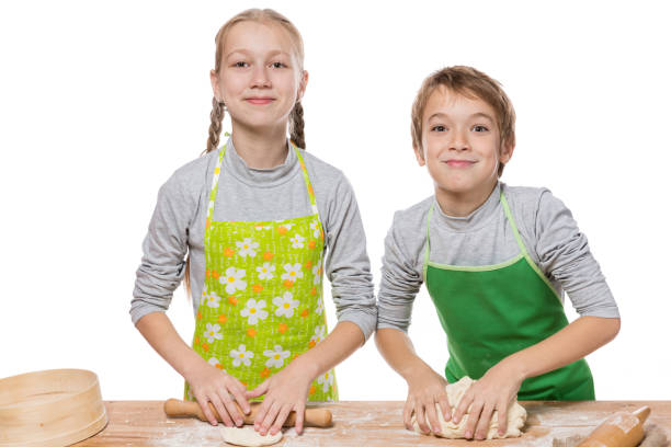 istock brother and sister roll out dough for baking and look at the camera, having fun, on white background, isolate 1018683980