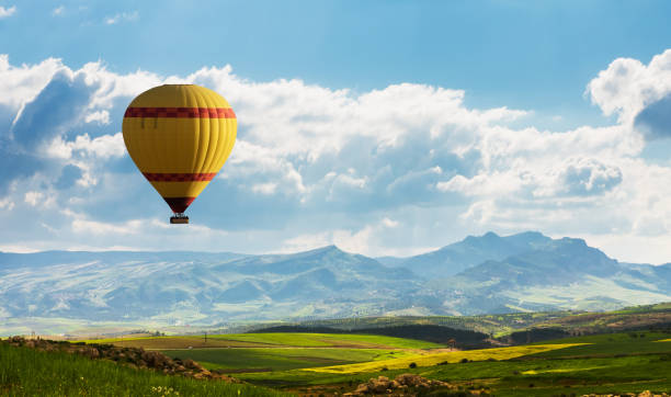 colorido globo aerostático volando sobre el campo verde - heat mid air flying float fotografías e imágenes de stock