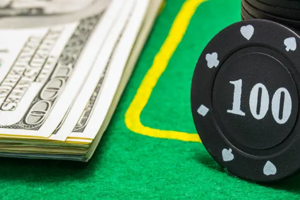 Photo of column of poker chips and a lot of dollar bills on a green canvas