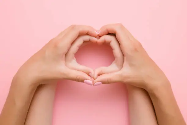 Photo of Heart shape created from little girl's hands and her mother's hands on the pink background. Lovely emotional, sentimental moment. Love, happiness and safety concept.