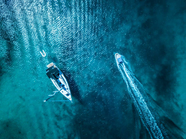 Anchored sailboat with rescue boat in shallow sea. Small motorboat passing by. High angle view photo from drone DJI Mavic Pro.