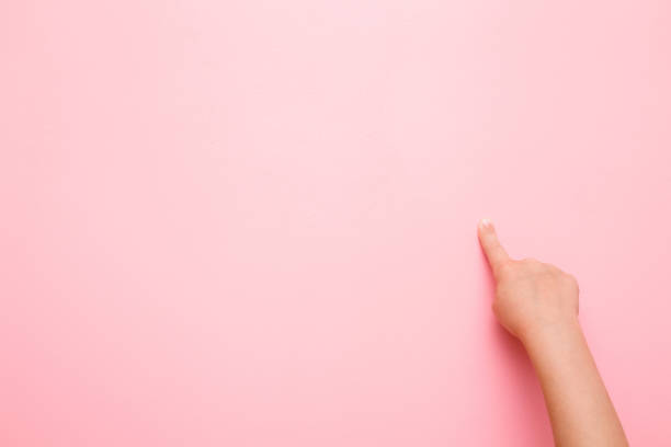 Little girl's finger pointing on the pink wall. Empty place for text or objects.