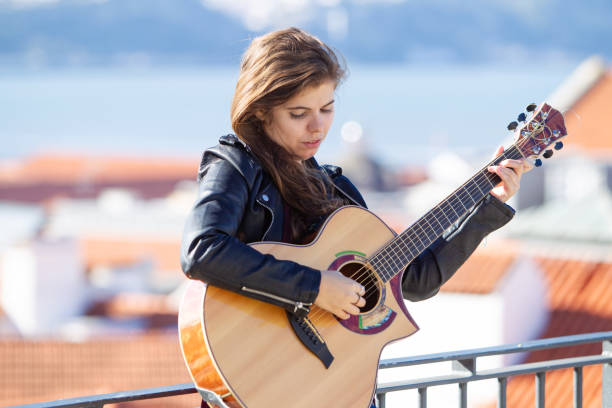 istock Serious young woman in black jacket playing guitar 1018707626
