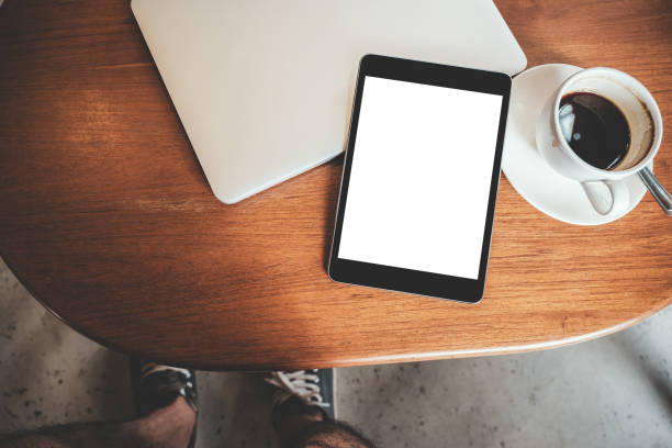 istock Top view mockup image of a black tablet pc with blank desktop white screen with laptop and coffee cup on wooden table 1018710816