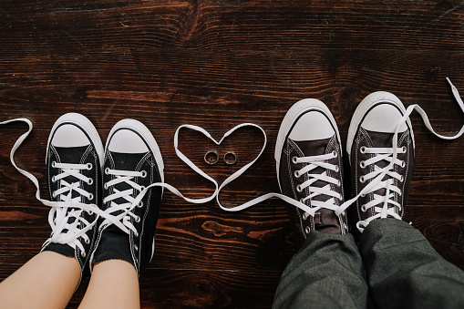feet of a loving couple in sneakers stand on a wooden floor. Hipster's  men's and women's feet