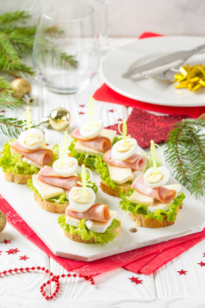 istock Christmas canapes on bread with brie or Camembert cheese, ham and boiled quail egg. Beautiful presentation on the festive new year's table. Delicious starter 1018732730