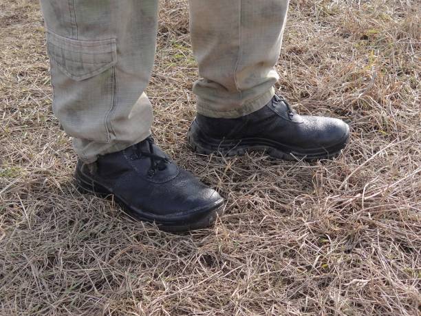 istock Black boots and legs in pants stand in dry gray grass 1018738542