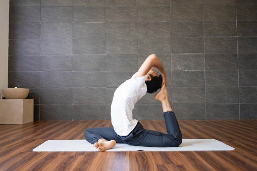 Indian yogi doing king pigeon yoga pose in gym. Man practicing advanced yoga. Yogi concept. Side view.