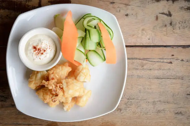 Top view of fried squid on a white plate on wooden with copy space.