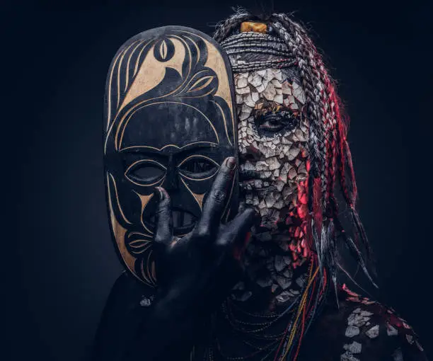 Close-up portrait of a witch from the indigenous African tribe, wearing traditional costume. Make-up concept. Isolated on a dark background.
