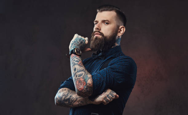 Pensive handsome old-fashioned hipster in a blue shirt and suspenders, standing with hand on chin in a studio. stock photo