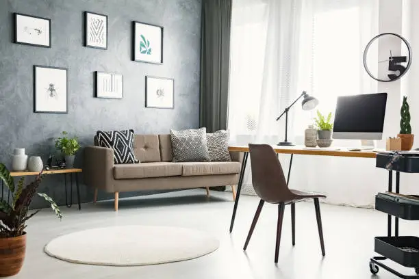 Photo of Real photo of a bright home office interior with a sofa, graphics, desk with a computer and lamp and modern clock