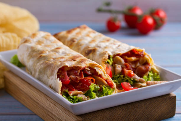 istock Chicken caesar salad wraps with bacon, tomatoes, lettuce and cheese. Tortilla, burritos, sandwiches twisted rolls 1018831628