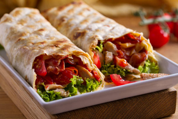 Chicken caesar salad wraps with bacon, tomatoes, lettuce and cheese. Tortilla, burritos, sandwiches twisted rolls