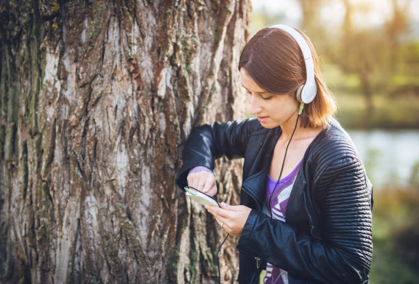istock Woman with headset standing next to tree and using mobile phone. 1018835260