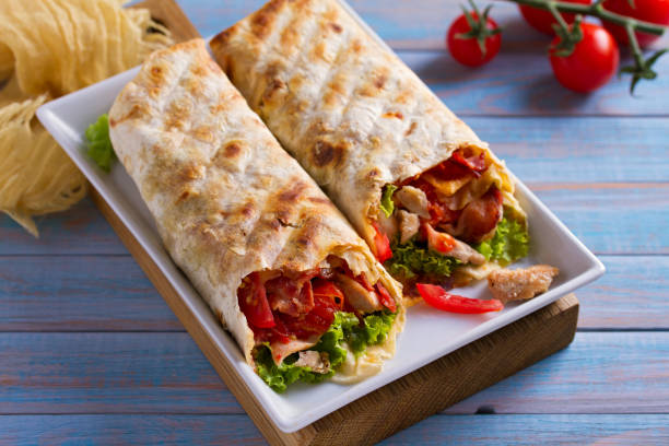 istock Chicken caesar salad wraps with bacon, tomatoes, lettuce and cheese. Tortilla, burritos, sandwiches twisted rolls 1018845892