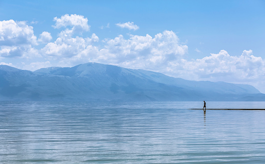 A silhouette of a man walking on a surface of a lake, with mountains in the distance and reflections in the water.