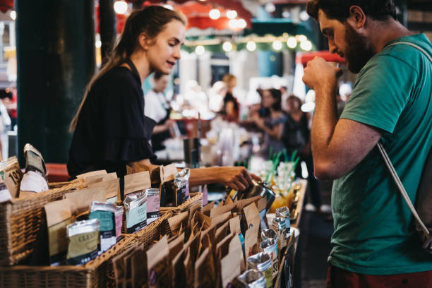 Seller and customer at a tea stand in Borough Market, London, UK. London, UK - July 24, 2018: Seller and customer at a tea stand in Borough Market, one of the largest and oldest food markets in London. Shallow focus. market trader stock pictures, royalty-free photos & images