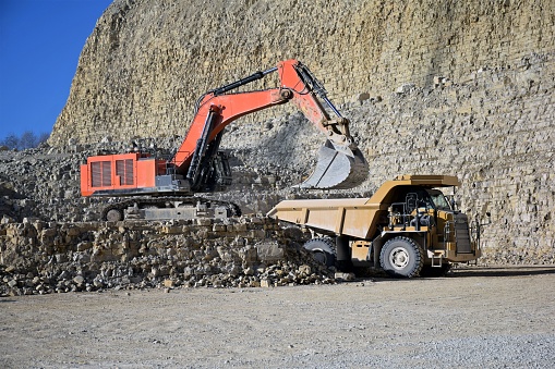 The excavator loads rocks onto the mining dump truck in the quarry area.