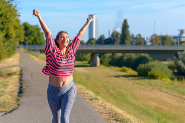 Happy fit woman cheering and celebrating Happy fit young woman cheering and celebrating as she walks along a river after working out jogging digestive system photos stock pictures, royalty-free photos & images