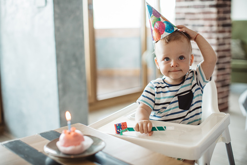 Little boy celebrate first birthday at home, wearing party hats, birthday cake and candle are ready