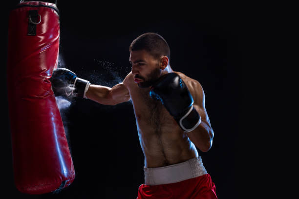 istock Bearded male boxer training with punching bag on black background. Male boxer as exercise for the big fight 1018939544