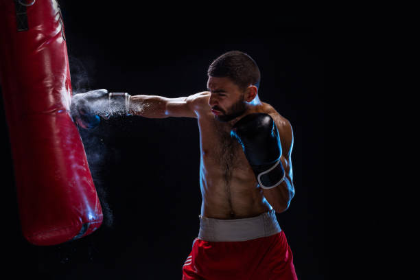istock Bearded male boxer training with punching bag on black background. Male boxer as exercise for the big fight 1018939560