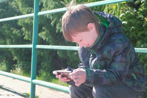 istock The boy plays a game on his mobile phone while sitting in the Park. 1018947680
