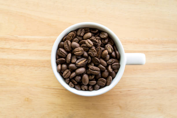 istock White coffee cup full of coffee beans on wood background 1018950934