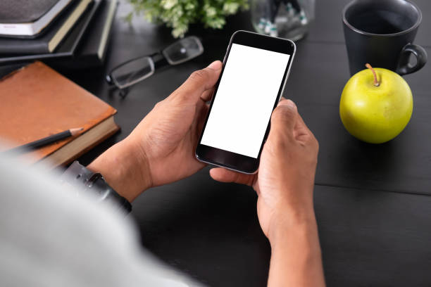 istock Man holding mockup smartphone on black table office workspace. 1018963180
