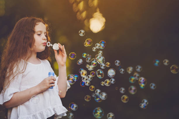 istock Little curly girl blowing soap bubbles. 1018972598