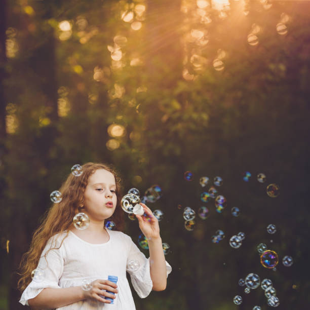 istock Little curly girl blowing soap bubbles. 1018972842