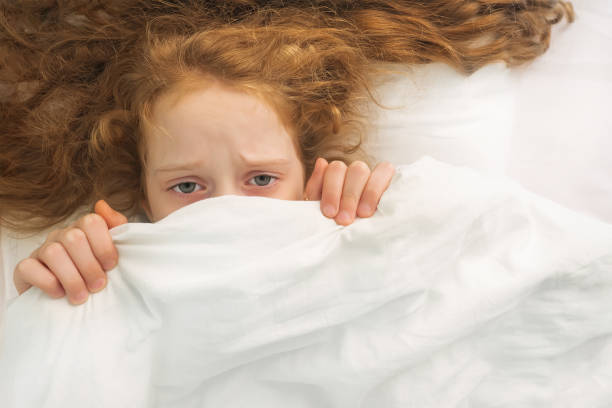istock Sad little girl afraid sleeping and pulling quilt on head. 1018975612