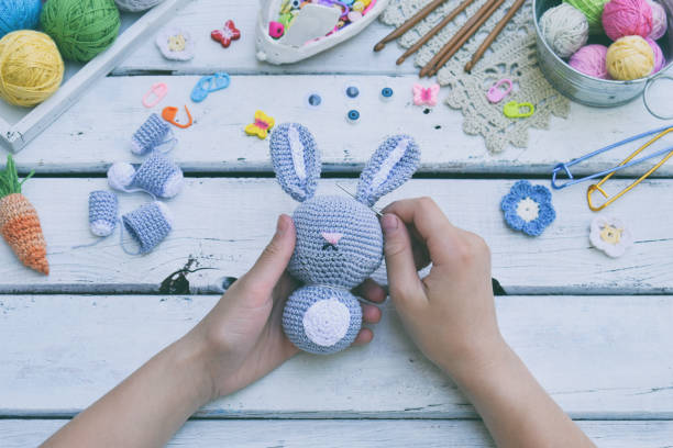 istock Making rabbit with carrot. Crochet bunny for child. On table threads, needles, hook, cotton yarn. Step 2 - to sew all details of toy. Handmade crafts. DIY concept. Small business. Income from hobby. 1018979600