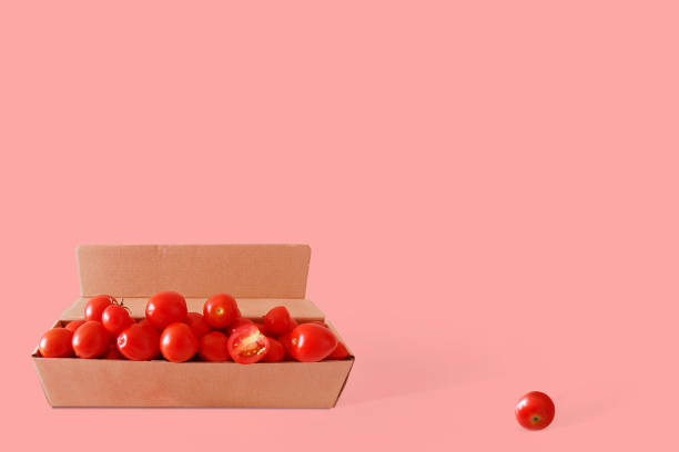 istock Red fresh cherry tomatoes in a cardboard box on a pink background. Creative image. Free space for text. 1018987670
