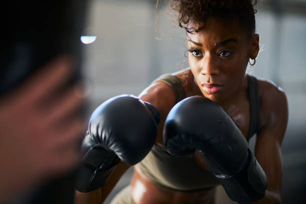 african woman boxing with punching bag in garage gym - boxing imagens e fotografias de stock