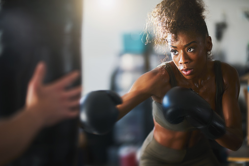 african american woman striking punching bag in home gym in fighting stance